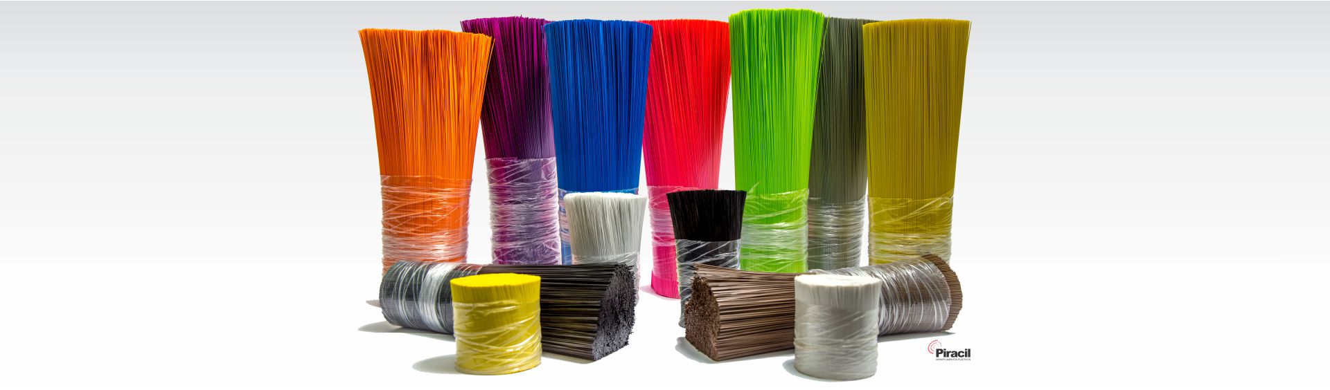 Feixes de monofilamento Piracil em laranja, roxo, azul, vermelho, verde, oliva, mostarda, preto, marrom e branco, de pé sobre fundo branco.