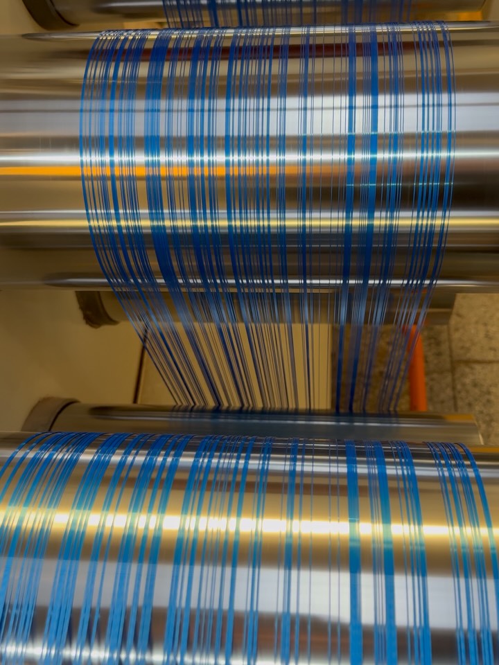 Monofilamento azul estabilizado saindo da linha de extrusão, sobre bobinas metálicas.